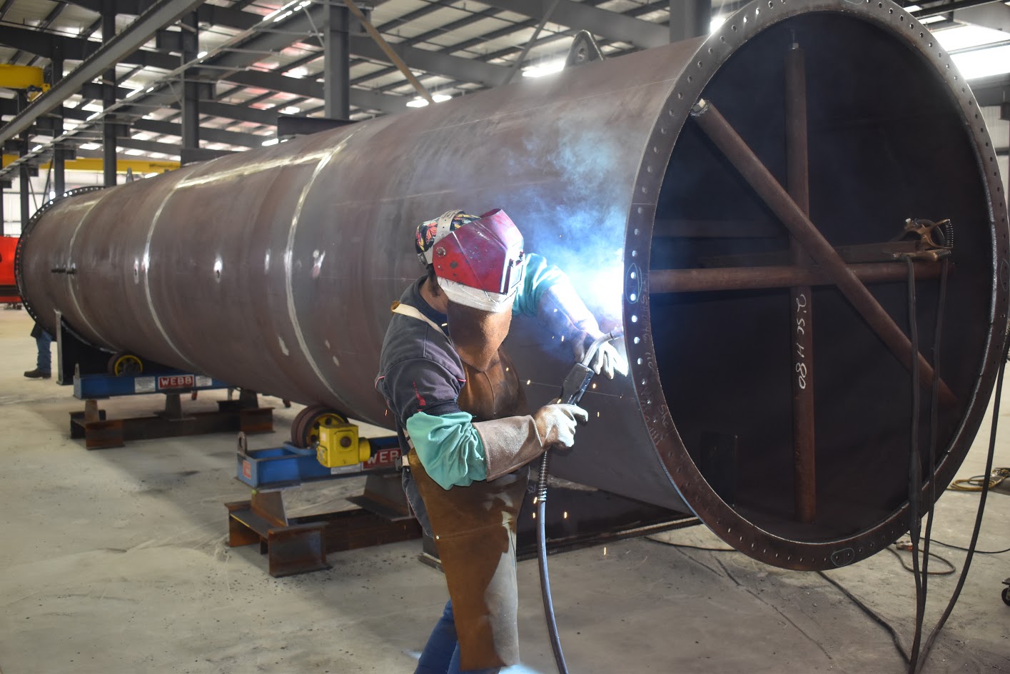A technician refurbishing the edges of a large steel tube